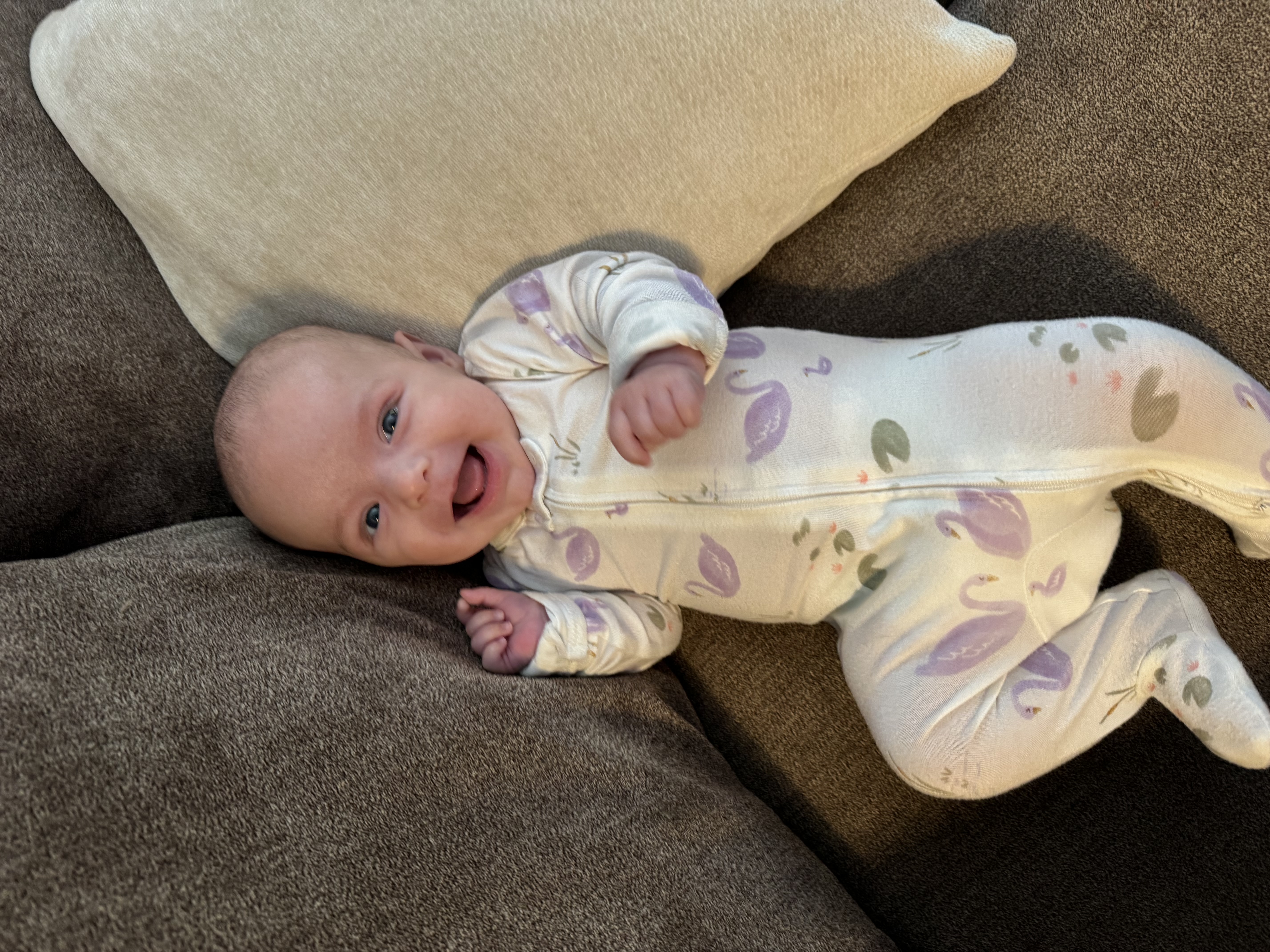A smiling baby lying on the couch, mid laugh