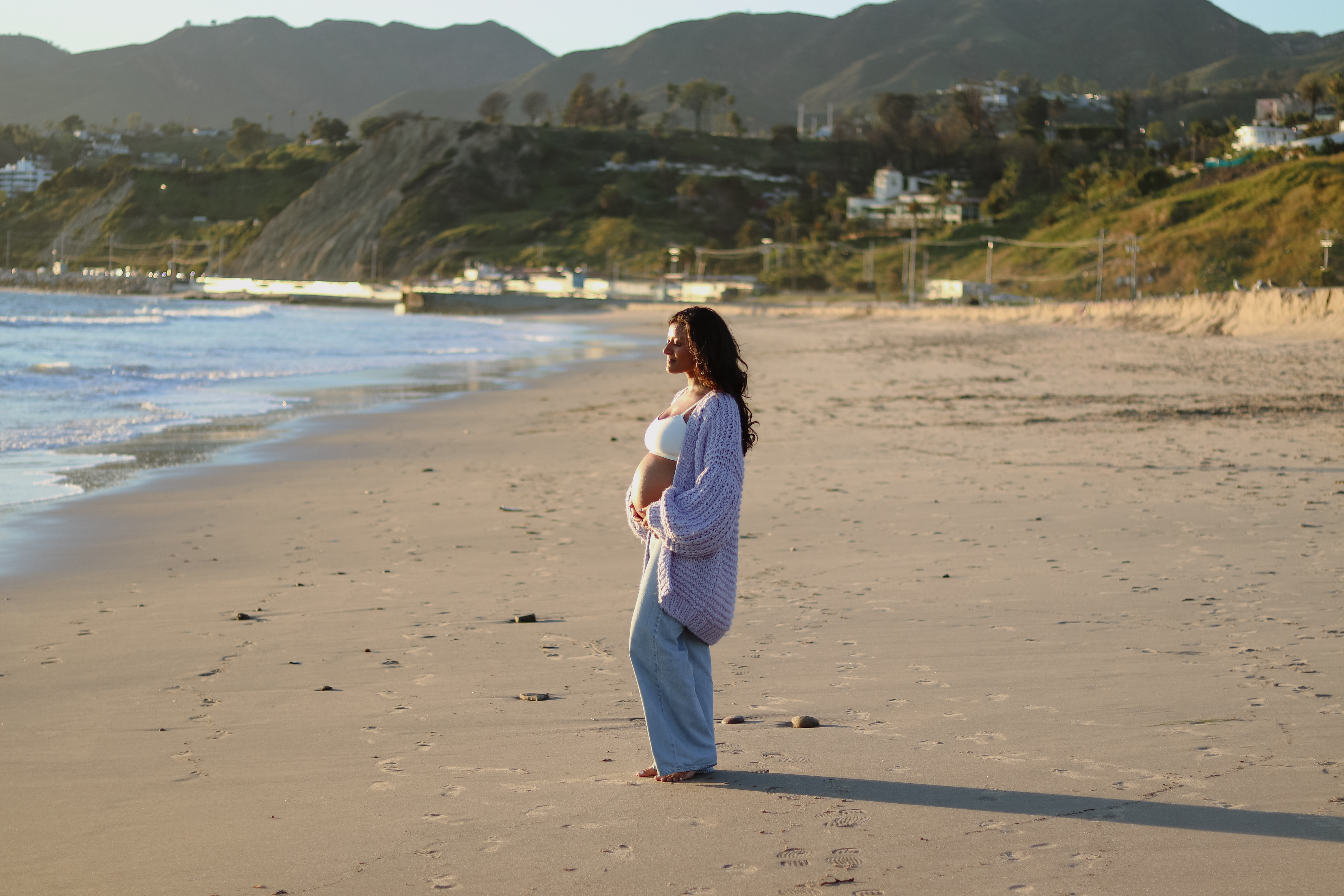 A pregnant mother standing on the beach at golden hour, cradling her belly
